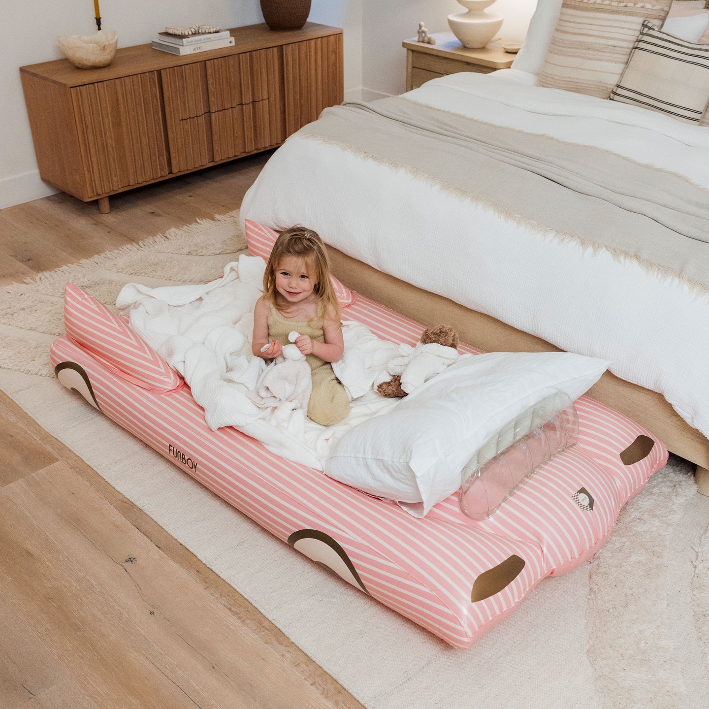 Child relaxing on a FUNBOY pink inflatable kids sleepover bed in cozy bedroom.