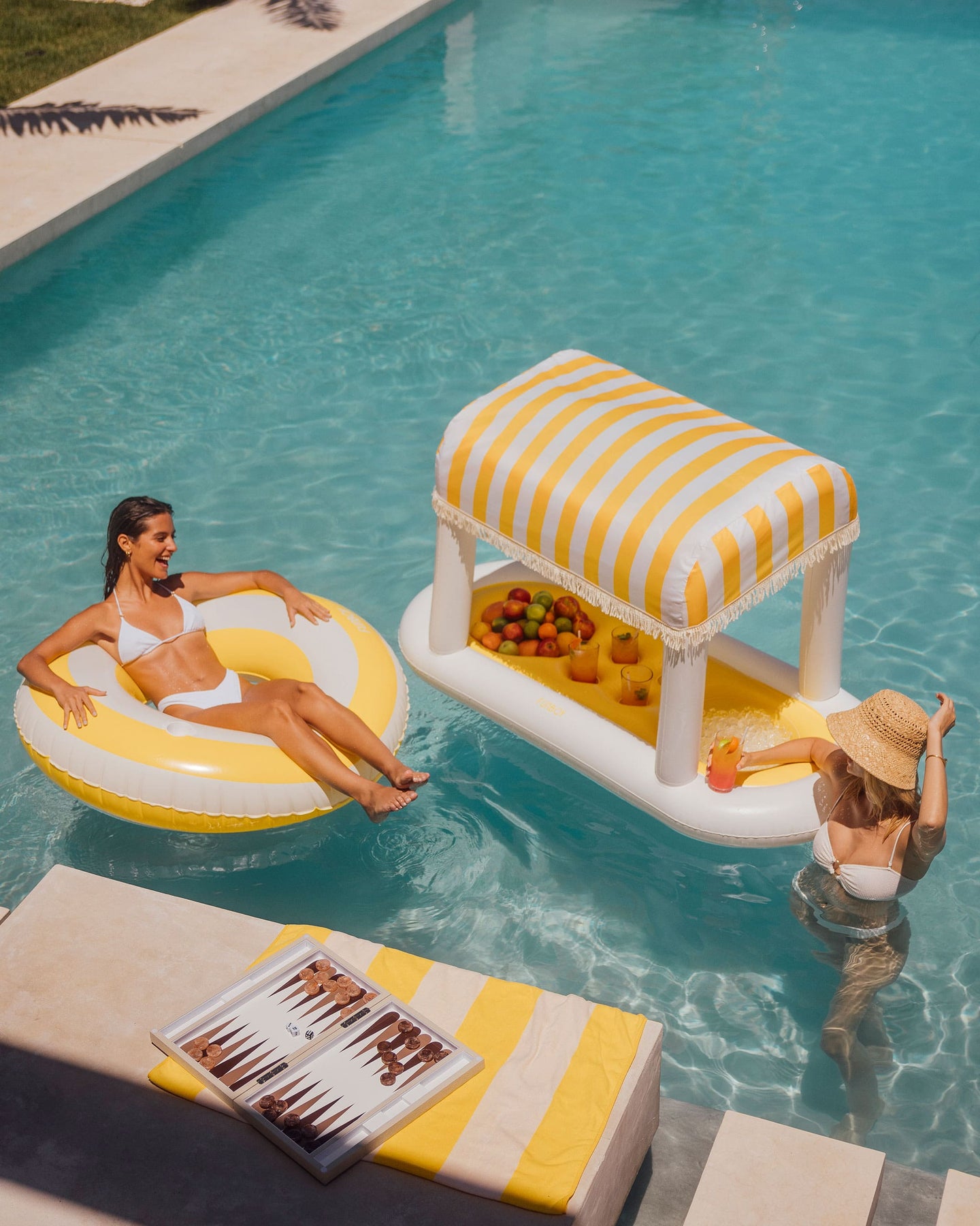 Poolside scene with FUNBOY inflatable lounger and floating drink bar. Relaxing under the sun by the pool.